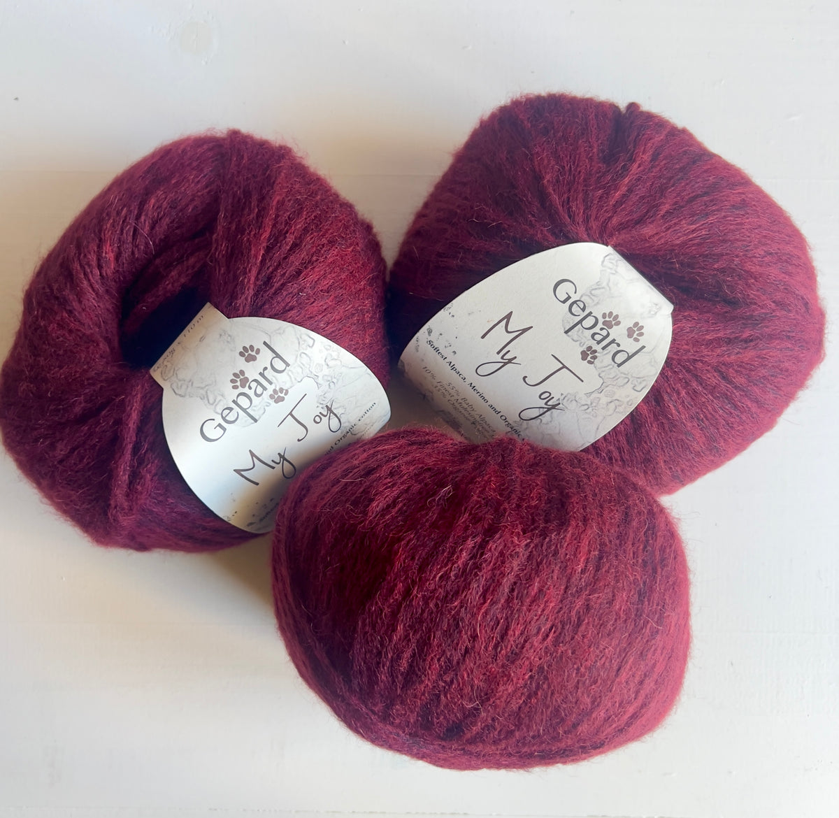 Three balls of Gepard My Joy yarn in 470 Black Cherry, a deep burgundy shade